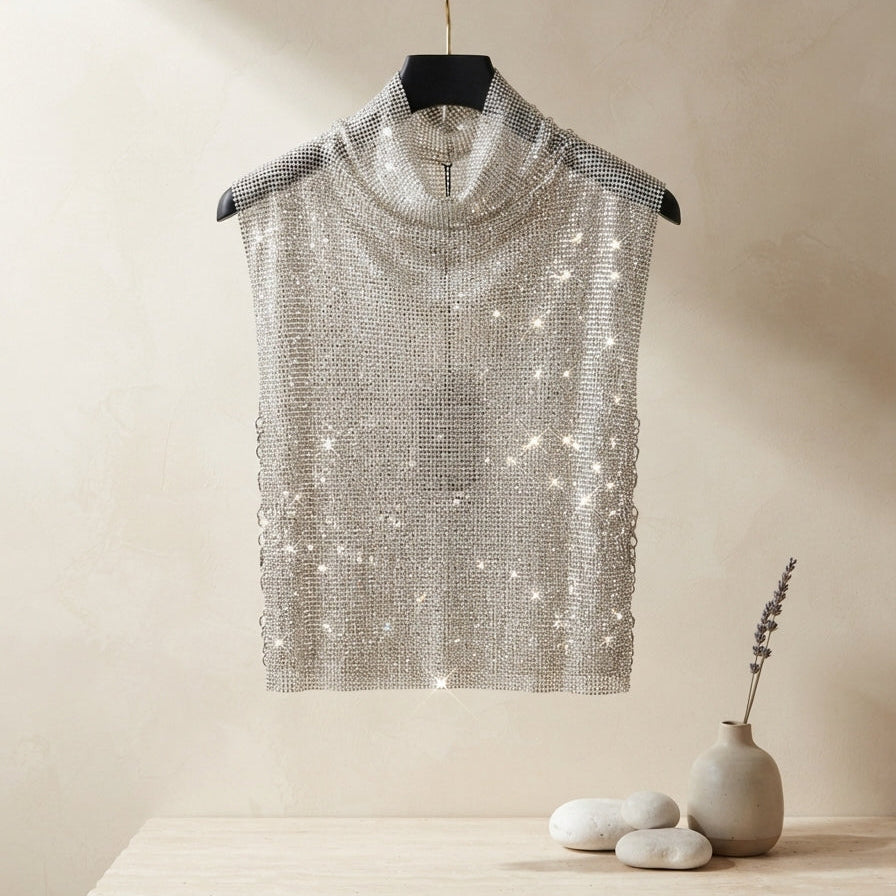 A sleeveless silver sequined mock-neck top hanging on a black hanger from a gold clothing rack, set against a warm beige textured wall with a rustic wooden shelf and small decorative vase below.