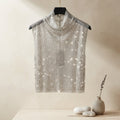 A sleeveless silver sequined mock-neck top hanging on a black hanger from a gold clothing rack, set against a warm beige textured wall with a rustic wooden shelf and small decorative vase below.